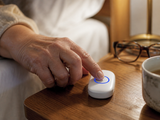 Elderly hand pressing the HomeChime call button on a nightstand
