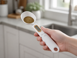 ScoopSense spoon scale held up in a kitchen, LCD display visible